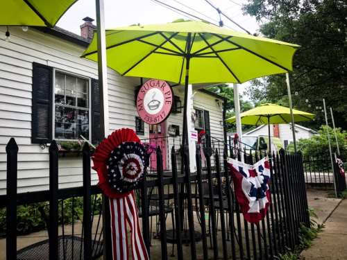 A charming café with bright green umbrellas, patriotic decorations, and a welcoming entrance.