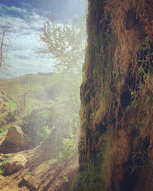 A sunlit scene of a rocky cliff with water mist and greenery, creating a serene, natural atmosphere.