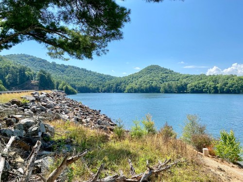 Scenic view of a calm lake surrounded by green hills and trees under a clear blue sky.
