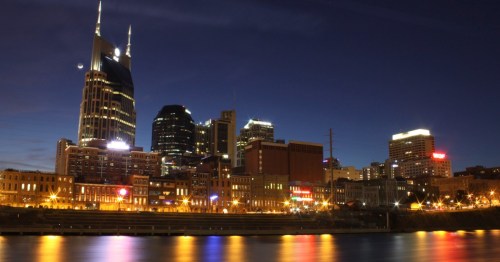 Nashville skyline at night, featuring illuminated buildings and reflections on the water.