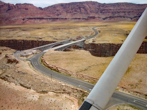 Aerial view of a bridge spanning a canyon, surrounded by rocky terrain and desert landscape.