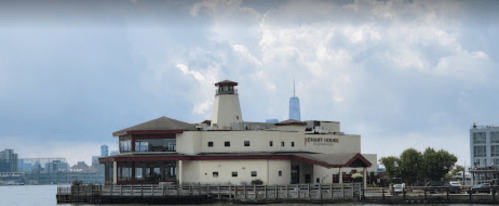 A waterfront restaurant with a lighthouse-style tower, surrounded by water and city skyline in the background.