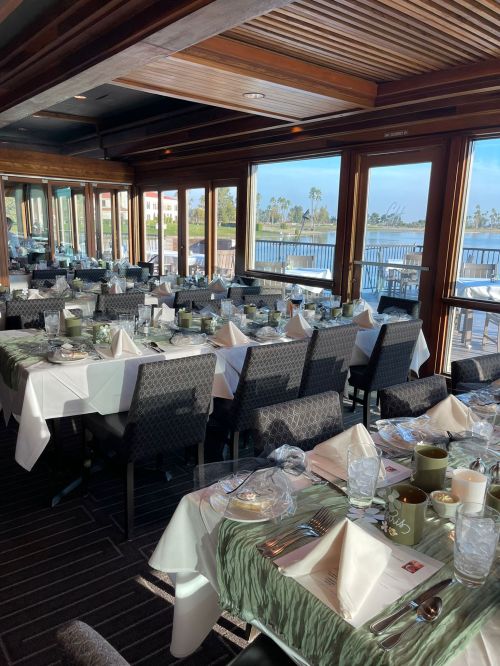 A beautifully set dining room with tables arranged for a meal, featuring elegant tableware and a view of the water.