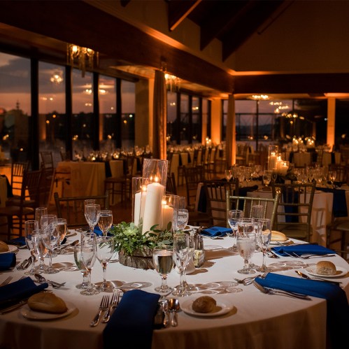 Elegant dining setup with candles and greenery, set for a formal event in a warmly lit venue.