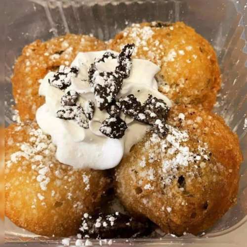 Fried dough balls topped with whipped cream and crushed chocolate, dusted with powdered sugar.