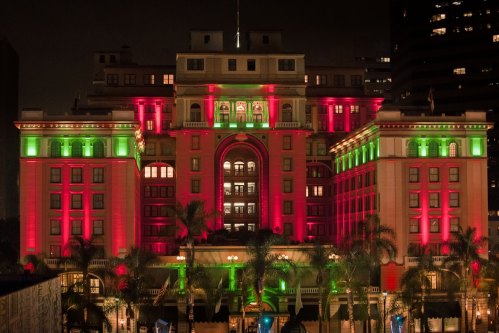 A brightly lit building at night, adorned with red and green lights, surrounded by palm trees.