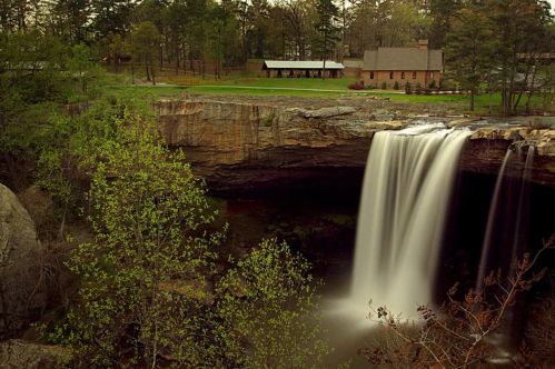A dramatic waterfall cascades over rocks with a pastoral view in the distance.