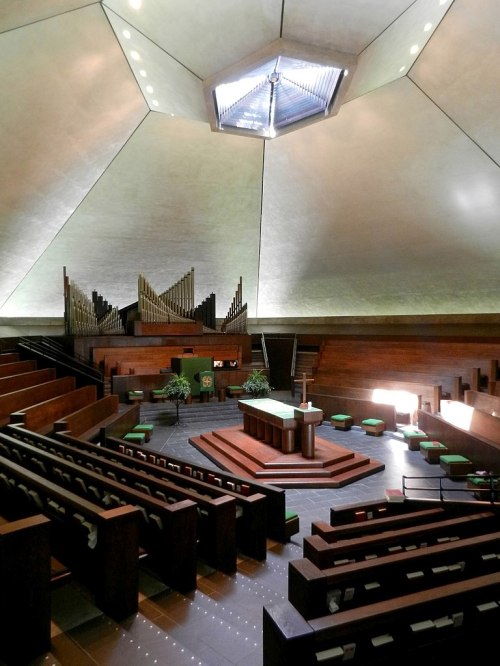 Interior of a modern church featuring a unique geometric ceiling, wooden pews, and an organ in the background.