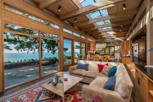 Bright, modern living room with large windows, a cozy sofa, and a view of the ocean and trees outside.