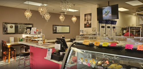 A cozy café interior with chandeliers, a display case of pastries, and a counter with seating.