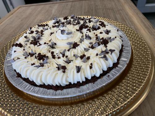 A chocolate cream pie topped with whipped cream and chocolate shavings, presented on a decorative gold plate.