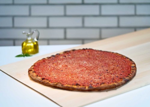 A large, round pizza with a thick crust and a rich tomato sauce topping, placed on a wooden surface with olive oil nearby.