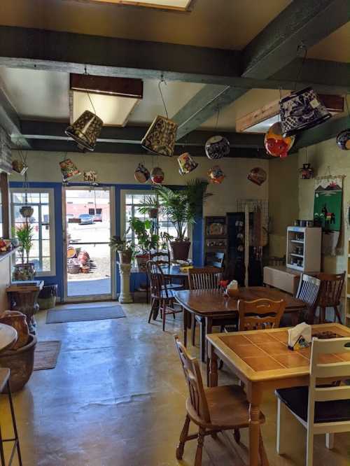 Cozy interior of a cafe with wooden tables, hanging decorations, and plants, leading to an outdoor view.