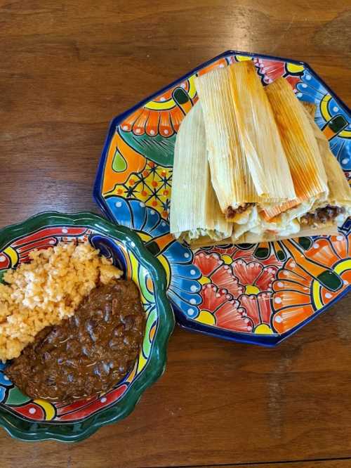 A colorful plate with tamales, rice, and beans, set on a vibrant, decorative table.