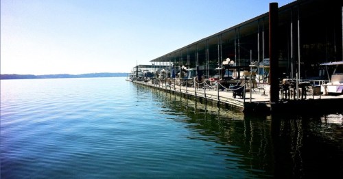 A calm waterfront scene featuring a dock with boats and a modern building under a clear blue sky.