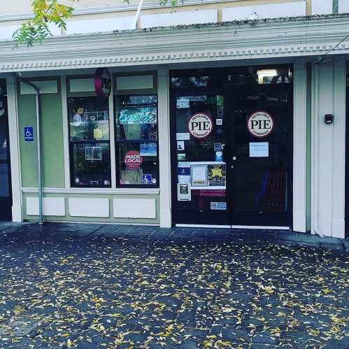 A storefront with "PIE" signs, featuring large windows and a door, surrounded by fallen leaves on the ground.