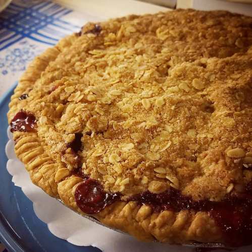A close-up of a homemade pie with a golden crust and a crumbly oat topping, resting on a blue plate.