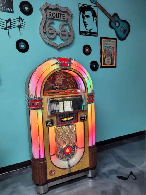 A colorful vintage jukebox with neon lights, set against a retro-themed wall featuring music decor.