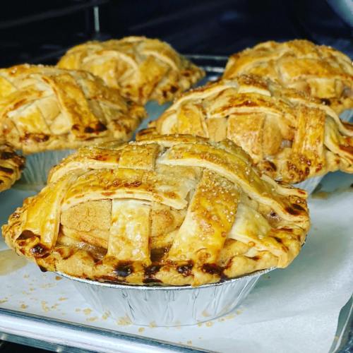 Four freshly baked mini apple pies with golden lattice crusts, sitting on a baking tray.
