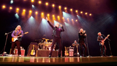 A rock band performs on stage with instruments and vibrant lighting, engaging the audience with energetic poses.