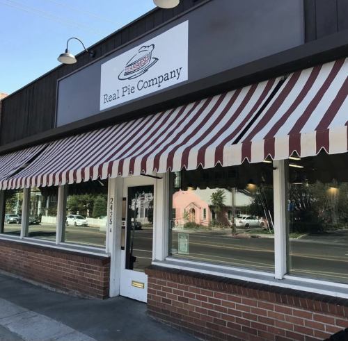 Exterior of Real Pie Company with a striped awning and large windows, showcasing a welcoming storefront.