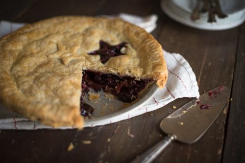 A freshly baked cherry pie with a slice removed, resting on a cloth napkin on a wooden table.