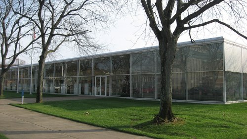 A modern glass building with a grassy area and bare trees in front, showcasing a minimalist architectural design.