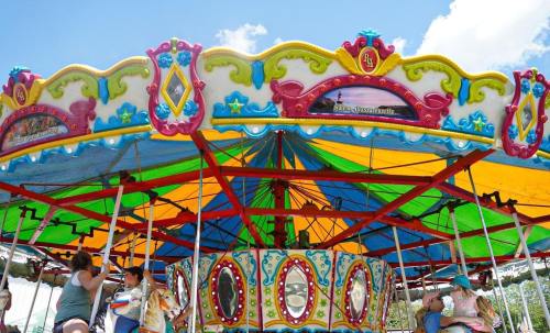 Colorful carousel with vibrant canopy, featuring riders enjoying the ride on a sunny day.