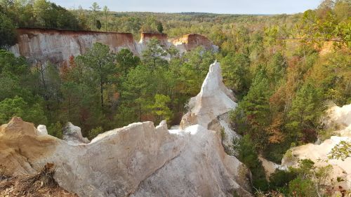 A scenic view of a canyon with white rock formations surrounded by lush green trees and rolling hills in the background.
