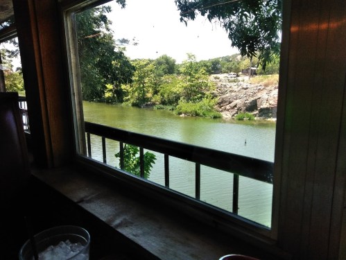 View from a window overlooking a serene river surrounded by lush greenery and rocky terrain.