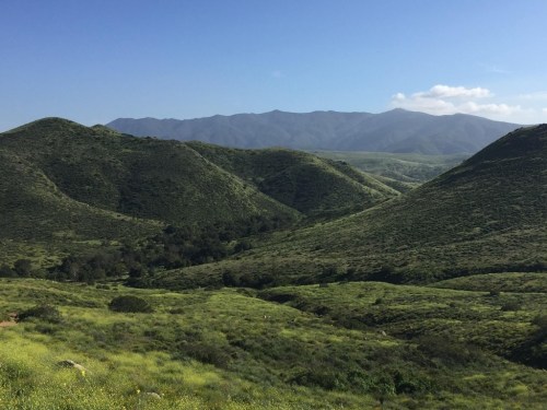 Lush green hills and mountains under a clear blue sky, showcasing a serene natural landscape.