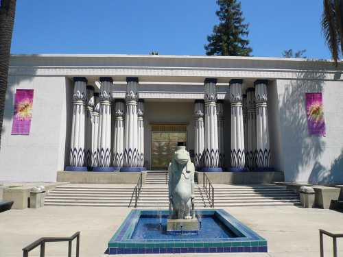 A modern building with Egyptian-inspired architecture, featuring columns and a lion statue in a fountain.