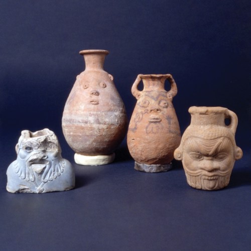 Four ancient pottery pieces with distinct facial features, set against a dark background.
