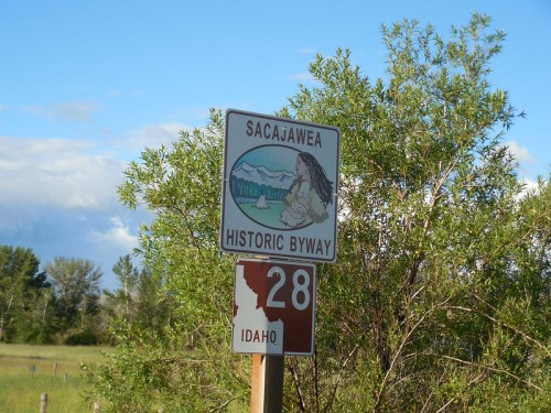 Sign for Sacajawea Historic Byway with an illustration and Idaho state marker, surrounded by greenery.