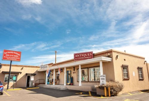 A single-story building with a sign reading "Antiques & Consignment," surrounded by a parking lot and blue sky.