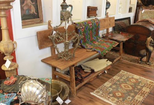 A vintage shop interior featuring wooden benches, decorative textiles, and various antique items on display.