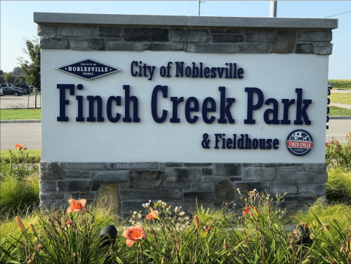 Sign for Finch Creek Park & Fieldhouse in Noblesville, featuring a stone base and colorful flowers in the foreground.
