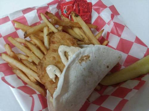 A plate of golden fries with a crispy fish fillet wrapped in a tortilla, drizzled with sauce, and a ketchup packet.