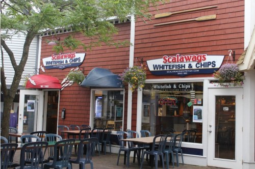 Exterior of Scalawags restaurant featuring "Whitefish & Chips" signage, outdoor seating, and hanging flower baskets.