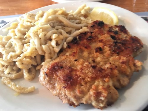 A plate featuring a golden-brown breaded chicken cutlet alongside a serving of creamy pasta and a lemon wedge.