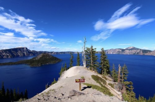 A scenic view of Crater Lake, featuring blue water, rocky shores, and lush trees under a clear sky.