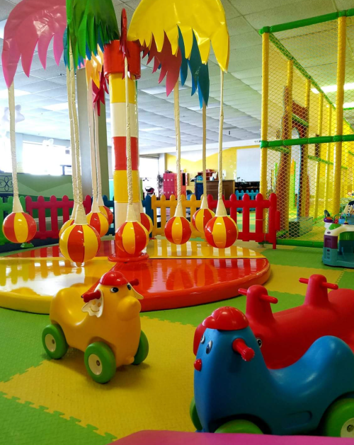 Colorful indoor play area with toy cars, palm trees, and soft flooring, designed for children's activities and fun.