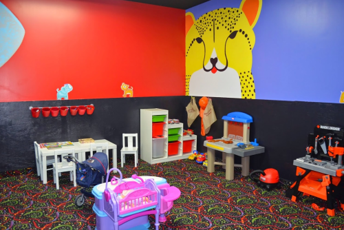 Colorful playroom with toys, a table, and a leopard mural on the wall. Brightly patterned carpet adds to the fun atmosphere.