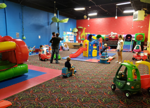 A colorful indoor play area with various toys, slides, and children playing with ride-on cars.