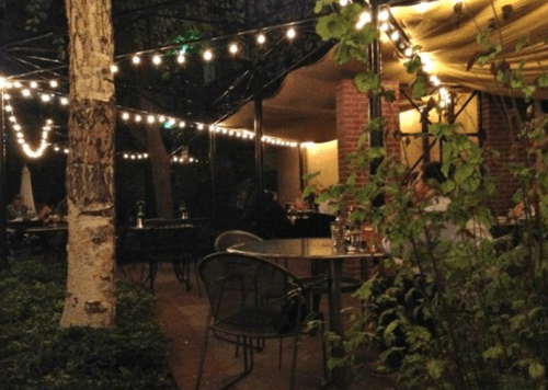 A cozy outdoor restaurant scene with string lights, tables, and greenery, creating a warm, inviting atmosphere.