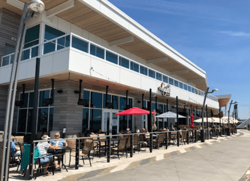A modern restaurant with outdoor seating, featuring umbrellas and patrons enjoying a sunny day.