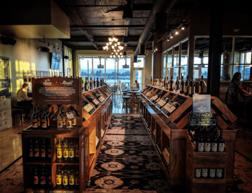 A cozy wine shop with wooden shelves displaying various bottles, warm lighting, and a view of the outdoors.