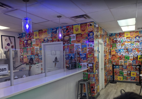 Colorful cereal-themed wall decor in a bright ice cream shop with a counter and neon sign.