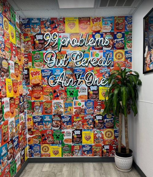 A colorful wall covered in cereal box designs with a neon sign that reads, "99 problems but cereal ain't one."