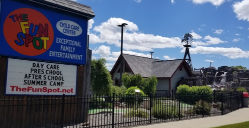 Sign for "The Fun Spot" child care center with a building and windmill in the background under a blue sky.